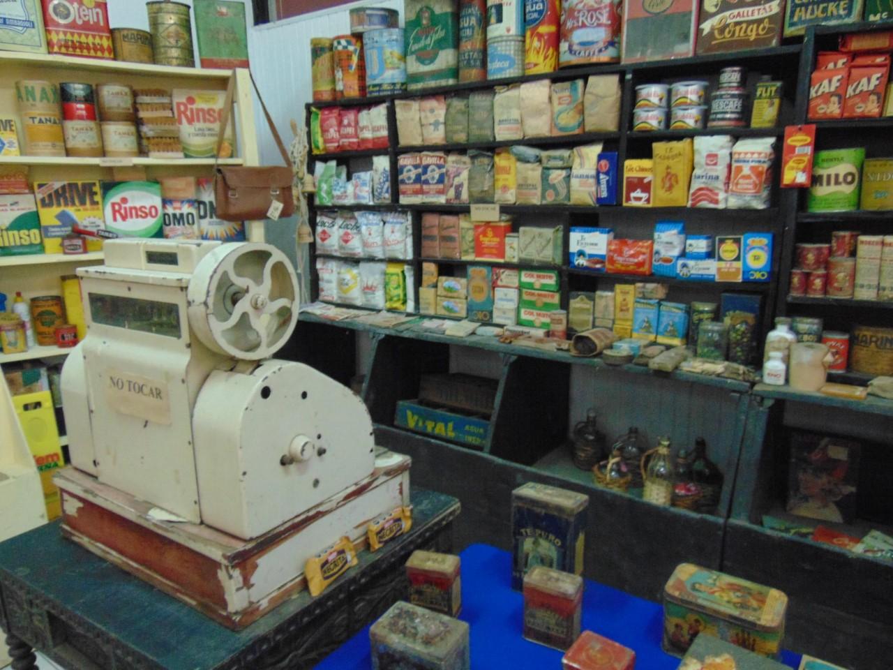 Fotografía de un almacén de barrio de los años 60', en la imagen se aprecia una antigua maquina registradora y góndolas con productos embasados.