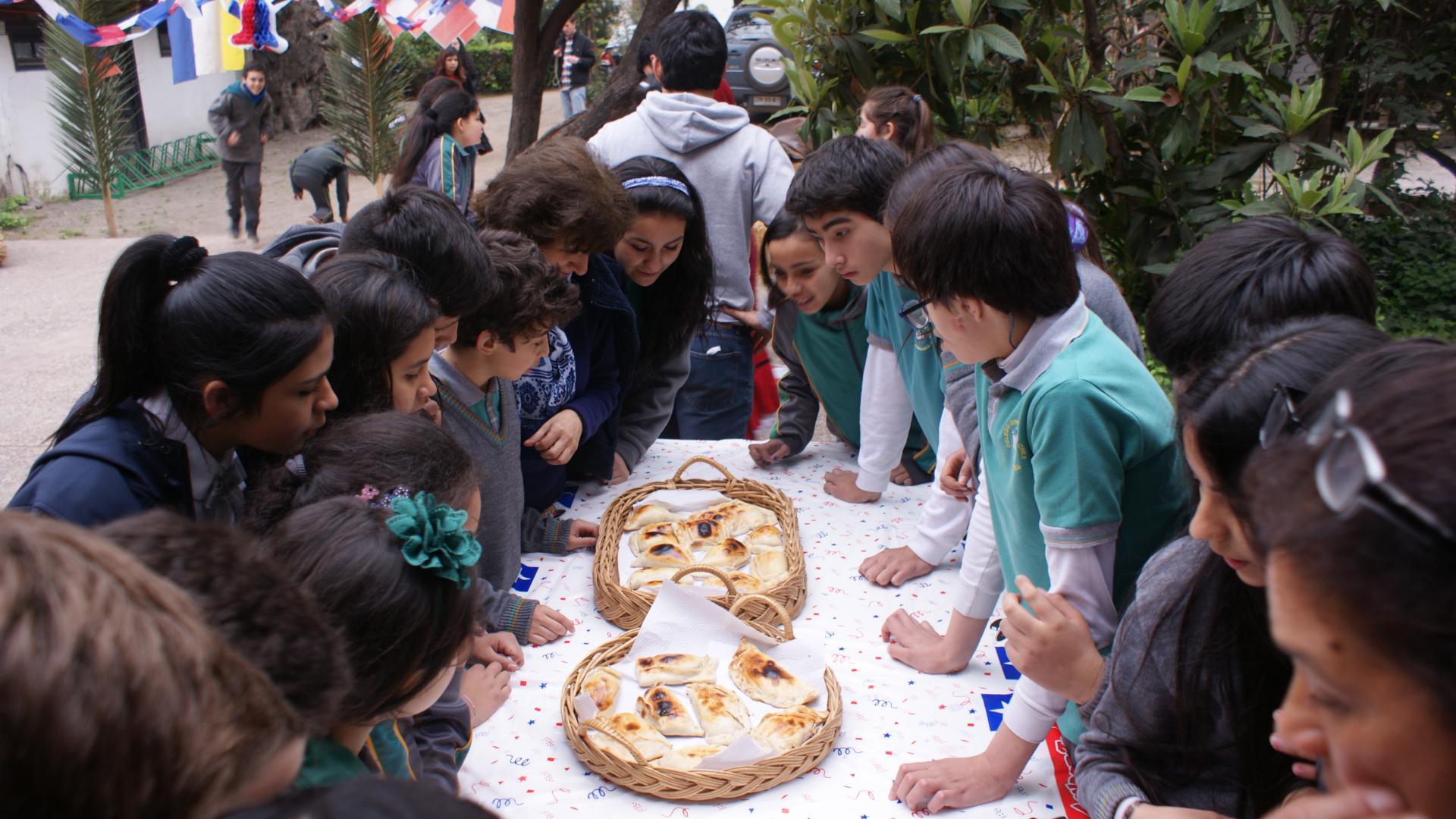 Niños y niñas rodeando una mesa que contiene canastas de empanadas de horno