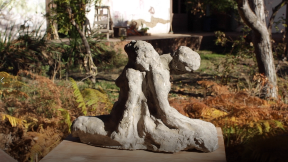 Escultura de piedra que ilustra dos cuerpos apoyados espalda con espalda, en evidente cansancio.