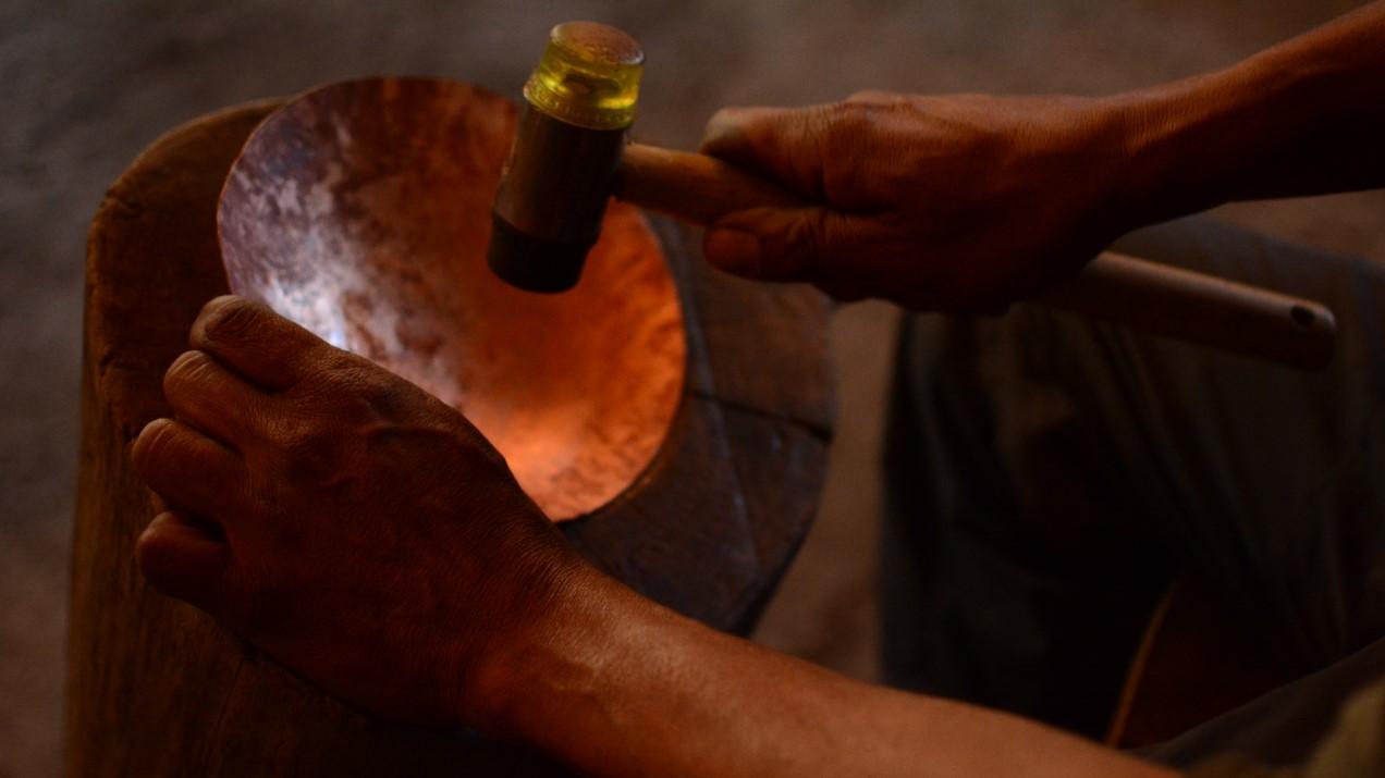 Fotografía que muestra una pieza de cobra en proceso de martillado, se aprecian unas manos golpeando la pieza con un martillo.
