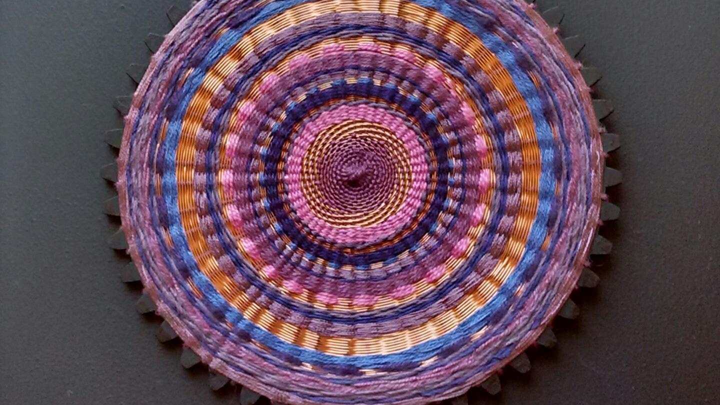 Artesanía textil circular en tonos morado y naranjas