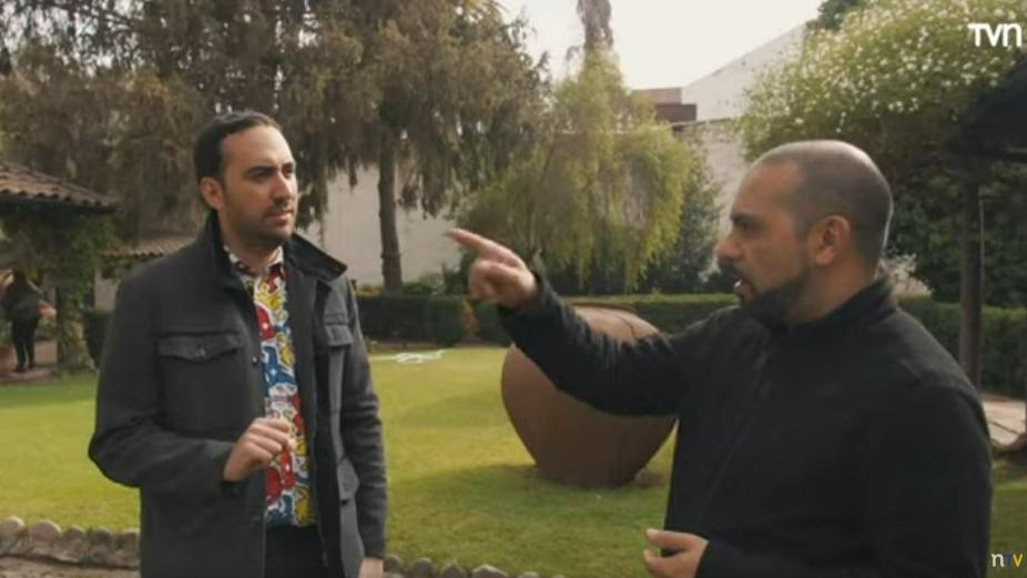 Imagen que muestra dos personas adultas conversando, en el fondo se aprecia un patio lleno de árboles y vegetación en tonos verdes. 