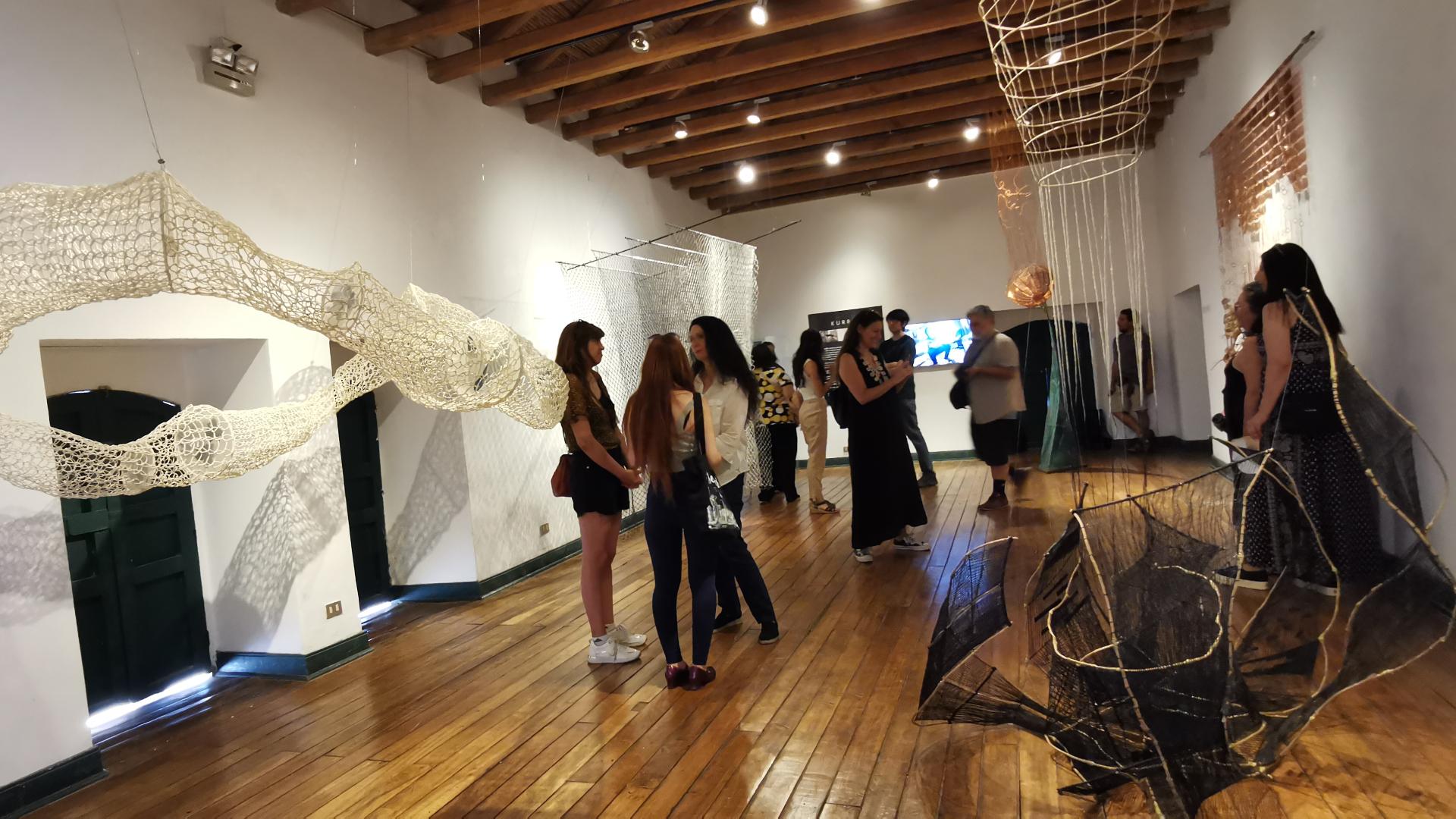 Sala de Exposición, con personas de pie conversando y las obras en exhibición