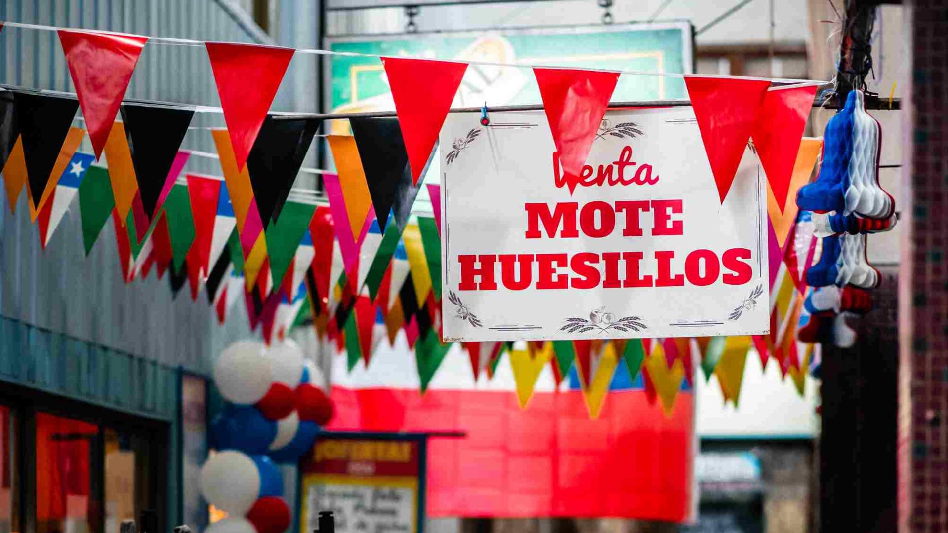 Muchos banderines de colores colgados y un letrero blanco con letras rojas que dice Mote con Huesillos
