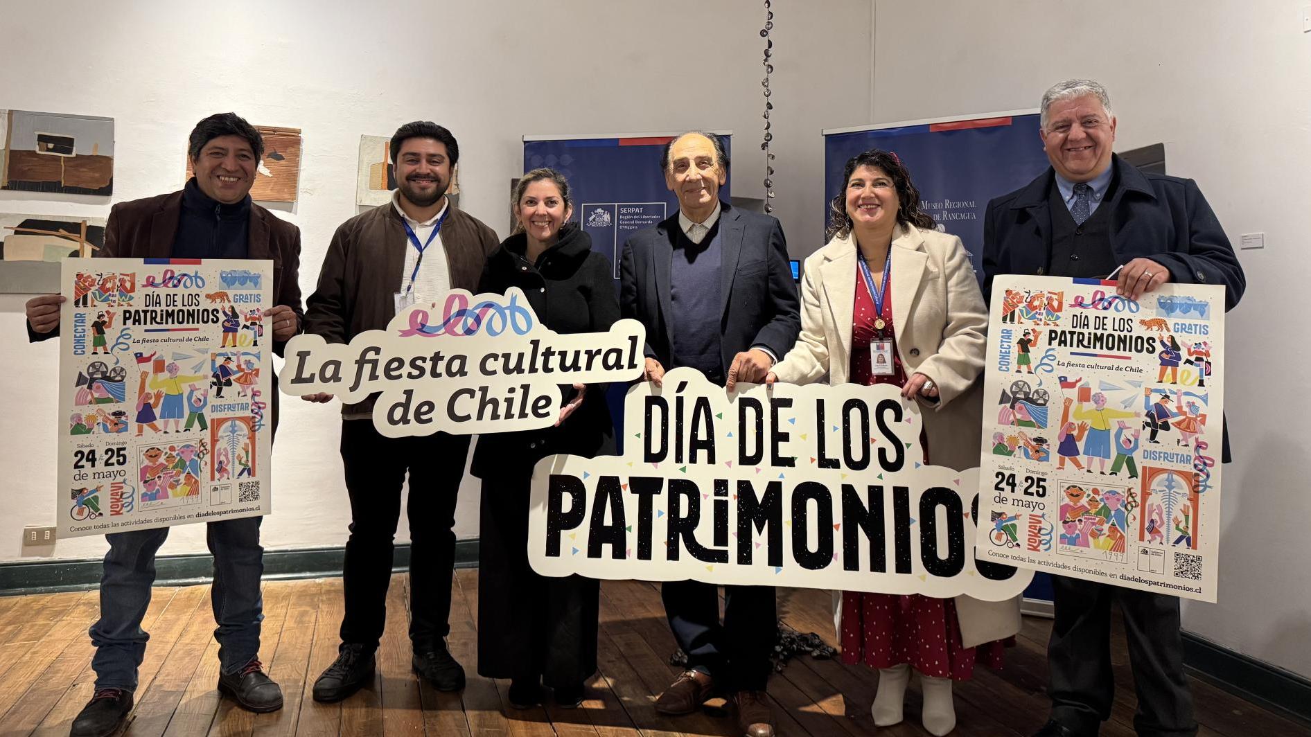 dos mujeres y cuatro hombres sonriuen para la fotografia mientras sostienen letreros que dicen dia de los patrimonios y la fiesta cultural de Chile