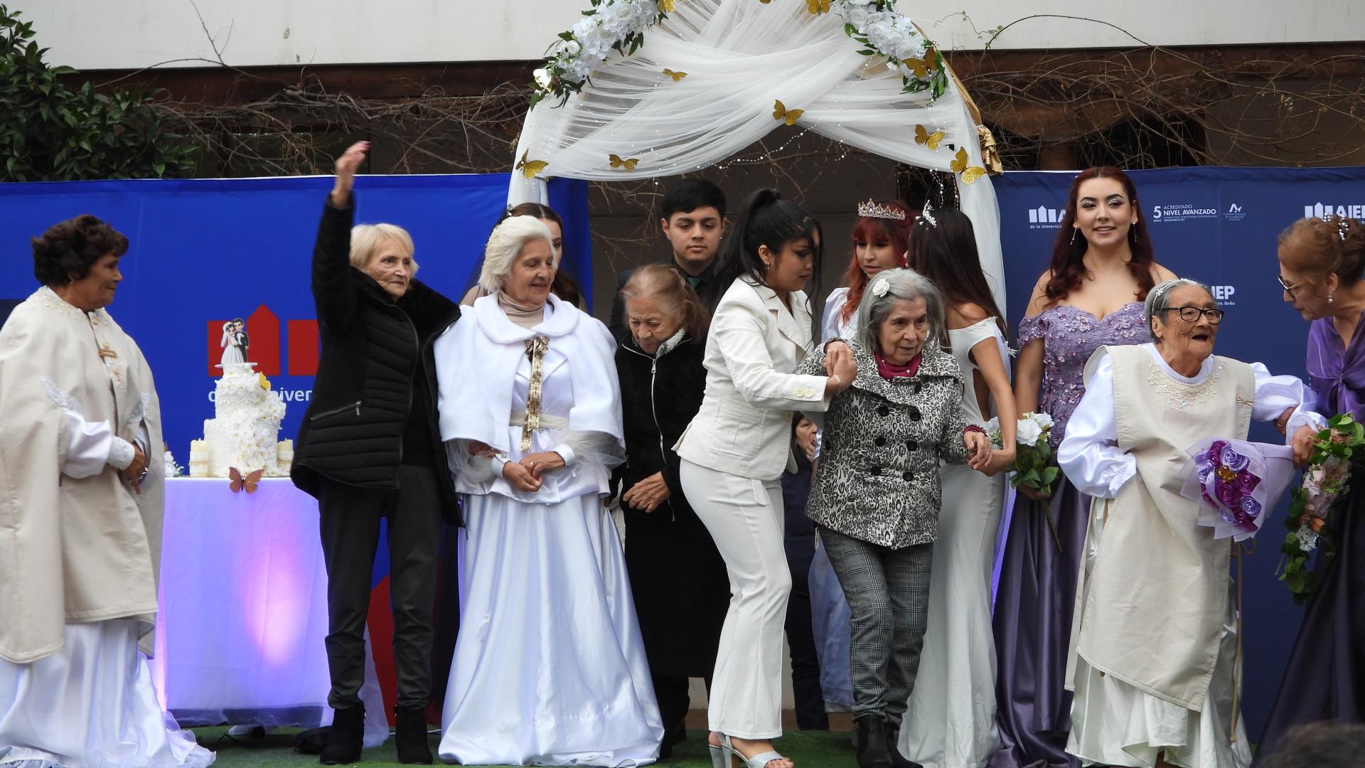 Mujeres ancianas y jóvenes vestidas de blanco con trajes de novia posan sobre un escenario