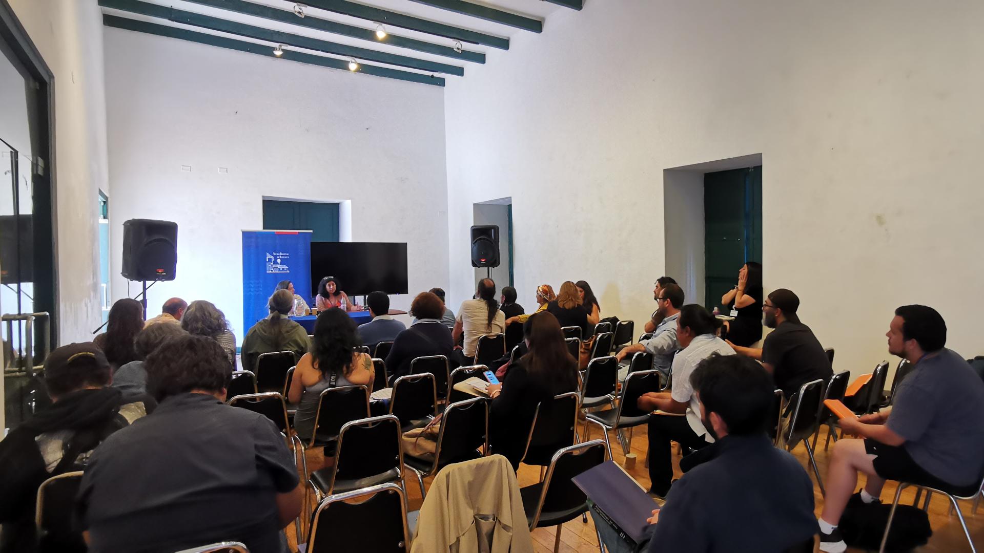 Salón con personas sentadas en sillas mirando hacia el fondo de la sala a una persona que presenta