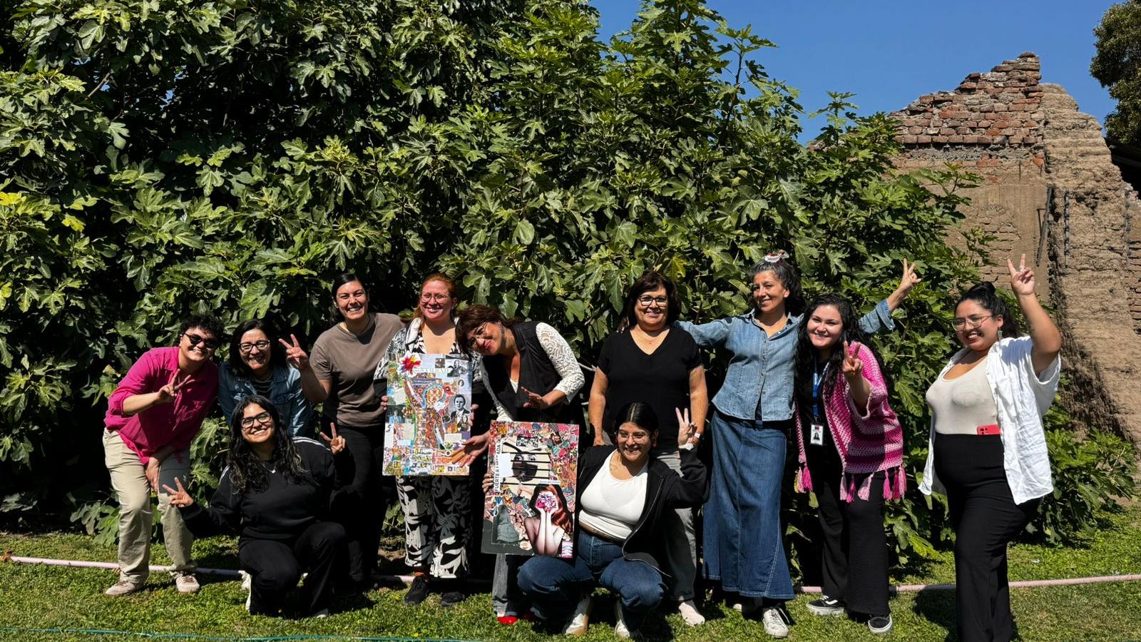 mujeres de pie frente a un arbol sonríen mientras posan para una foto y saludan a la camara