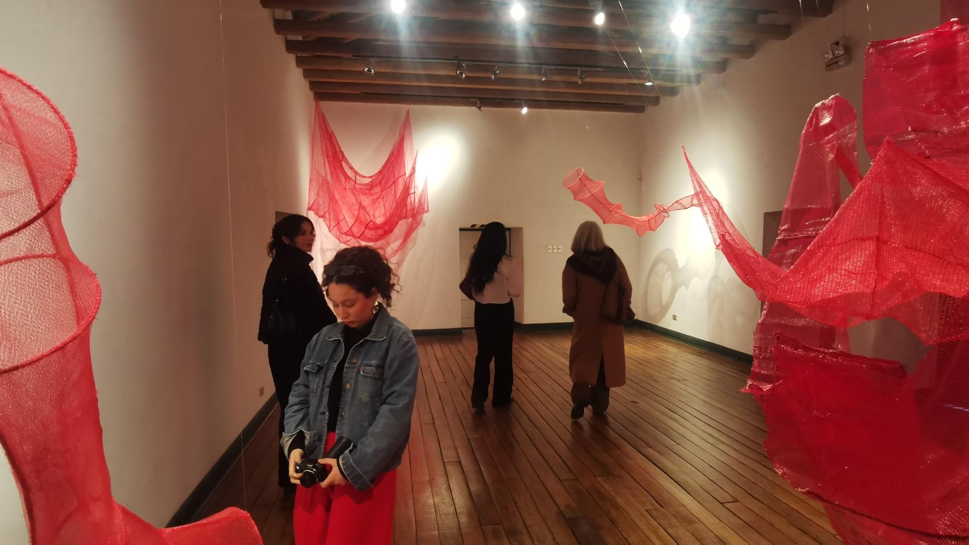 Sala de museo con esculturas aereas en color rojo y personas recorriendo la sala