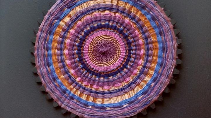 Artesanía textil circular en tonos morado y naranjas 