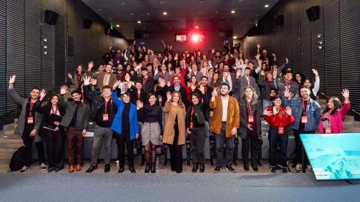 personas de pie en un teatro, saludan con la mano en alto