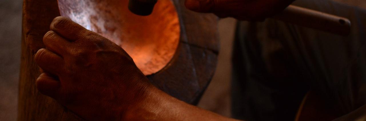 Fotografía que muestra una pieza de cobra en proceso de martillado, se aprecian unas manos golpeando la pieza con un martillo.
