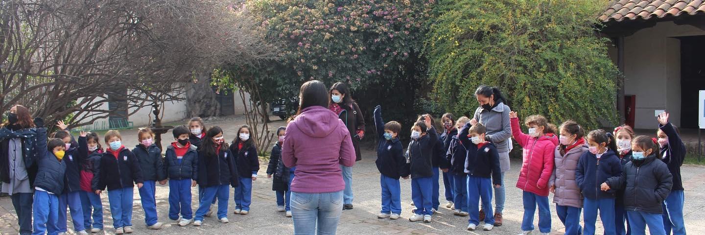 Se aprecia un grupo de niños y niñas junto a sus educadoras disfrutando de una visita mediada, algunos de estos infantes entusiasmados levantan su mano para responder una pregunta.