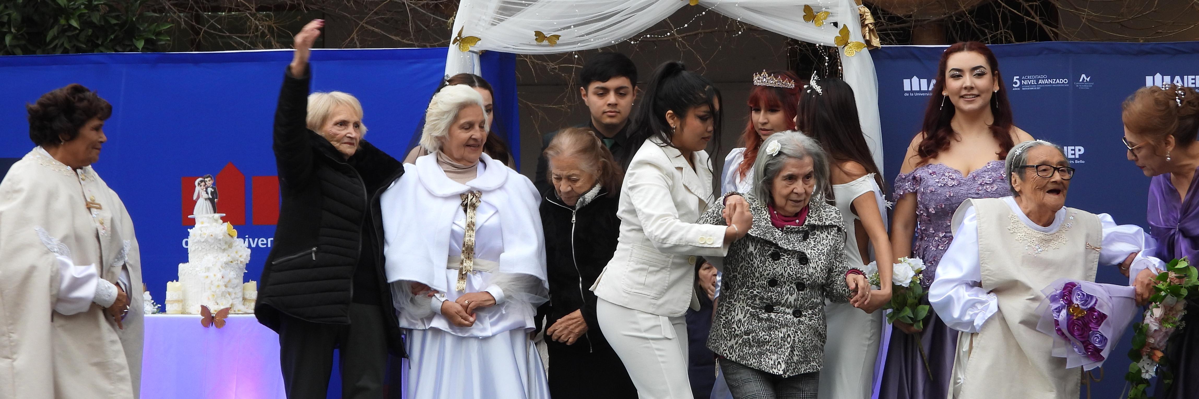 Mujeres ancianas y jóvenes vestidas de blanco con trajes de novia posan sobre un escenario