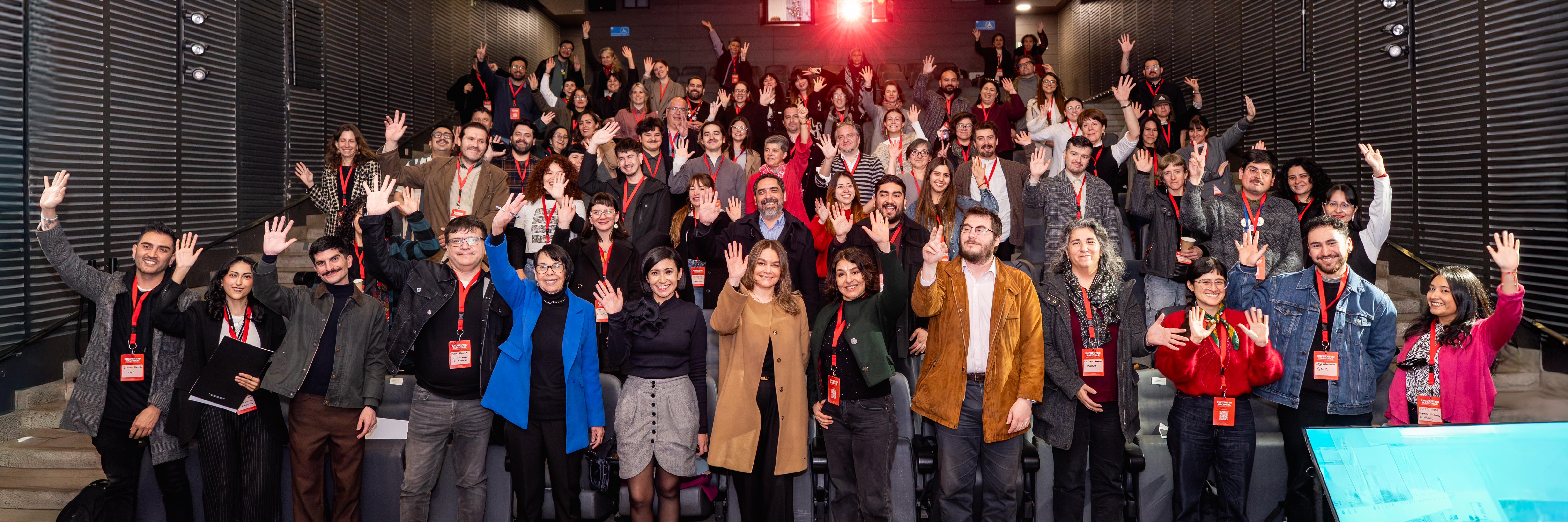 personas de pie en un teatro, saludan con la mano en alto