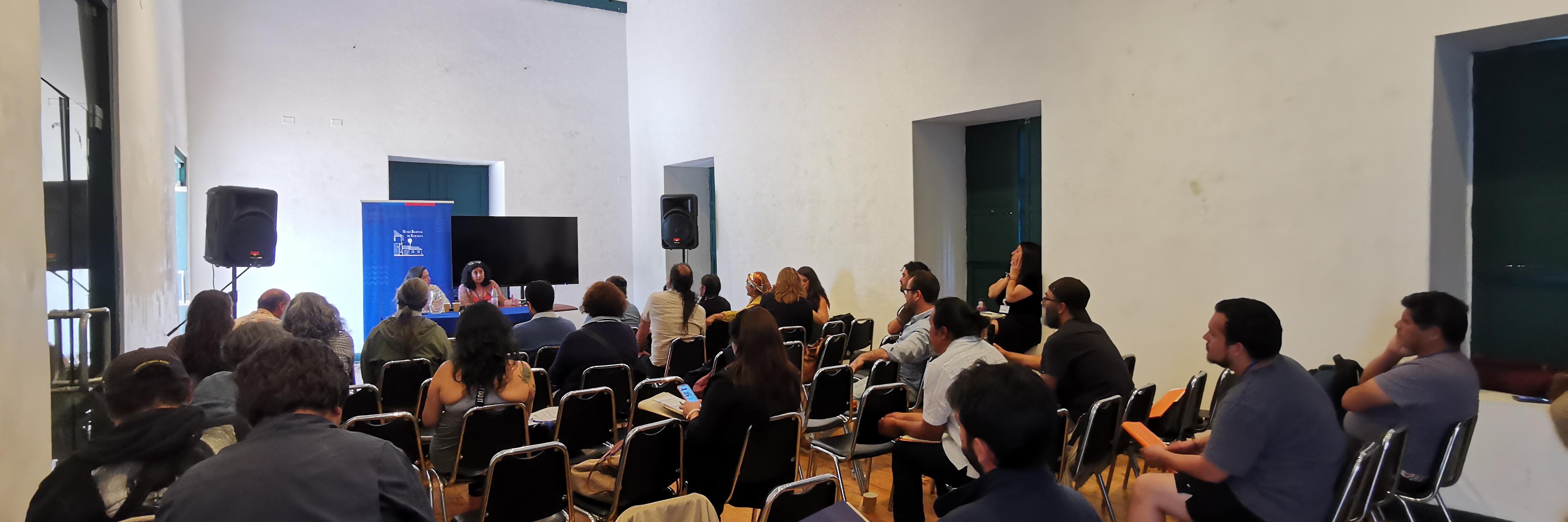 Salón con personas sentadas en sillas mirando hacia el fondo de la sala a una persona que presenta