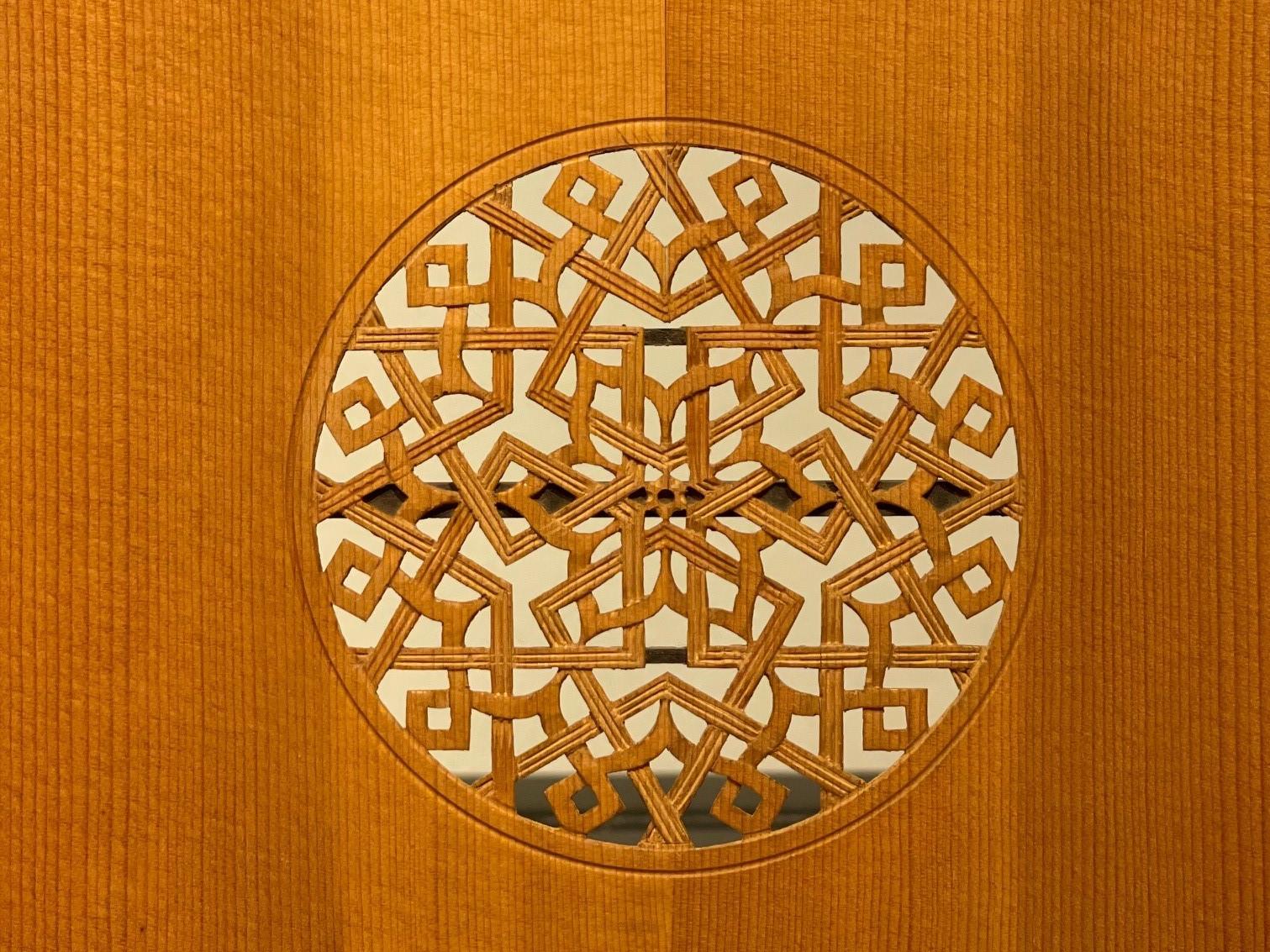 En la imagen se aprecia una lámina de madera tallada, que corresponde a la cara frontal de un laud, en su centro se observa un círculo calado con motivos florales y geométricos.