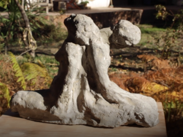 Escultura de piedra que ilustra dos cuerpos apoyados espalda con espalda, en evidente cansancio. 