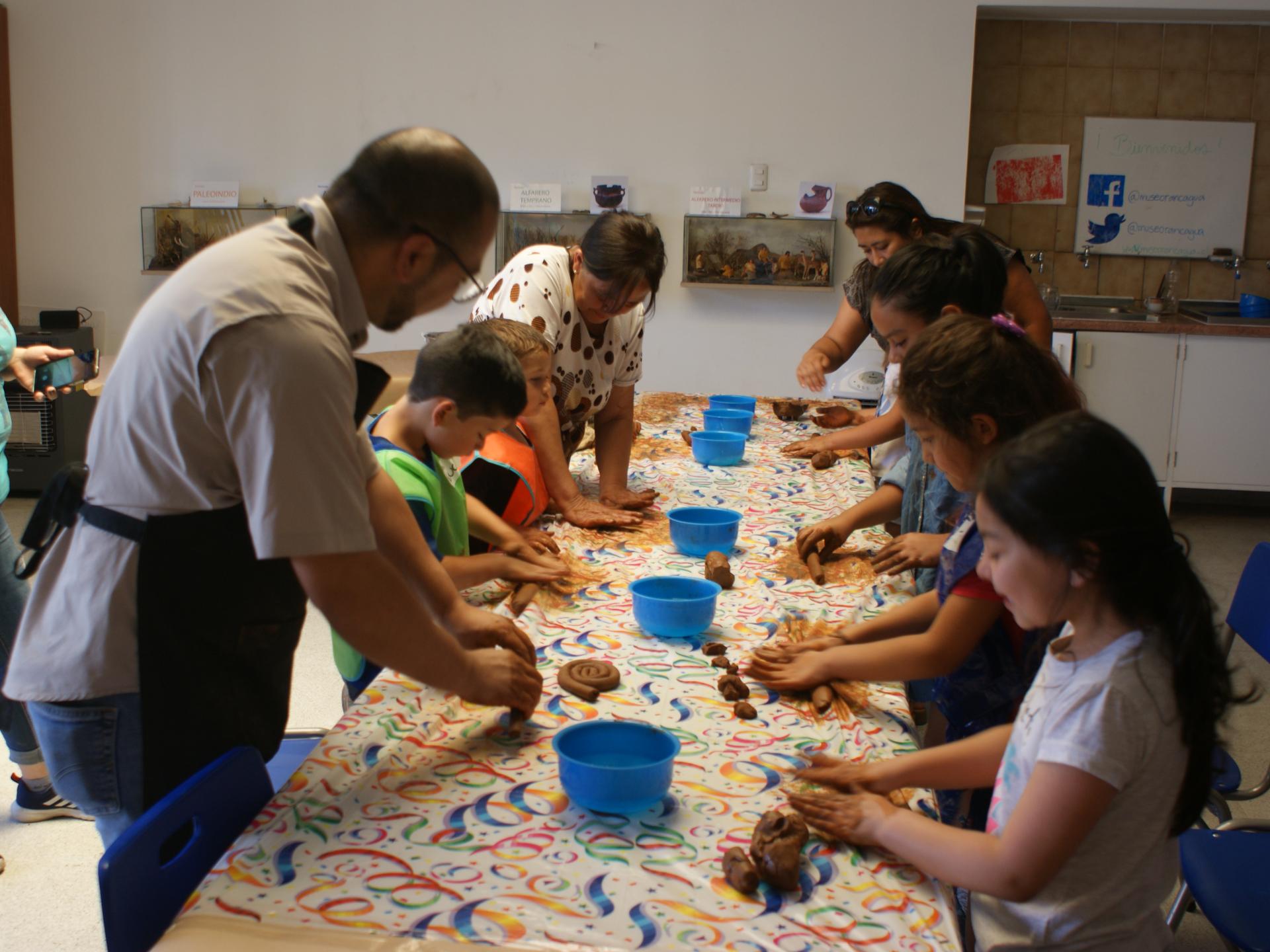 Fotografía panorámica que muestra un grupo de niños, niñas y adultos realizando un modelado en greda. 