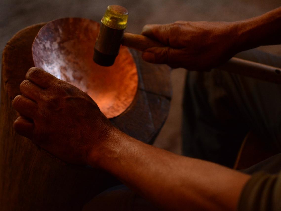 Fotografía que muestra una pieza de cobra en proceso de martillado, se aprecian unas manos golpeando la pieza con un martillo.