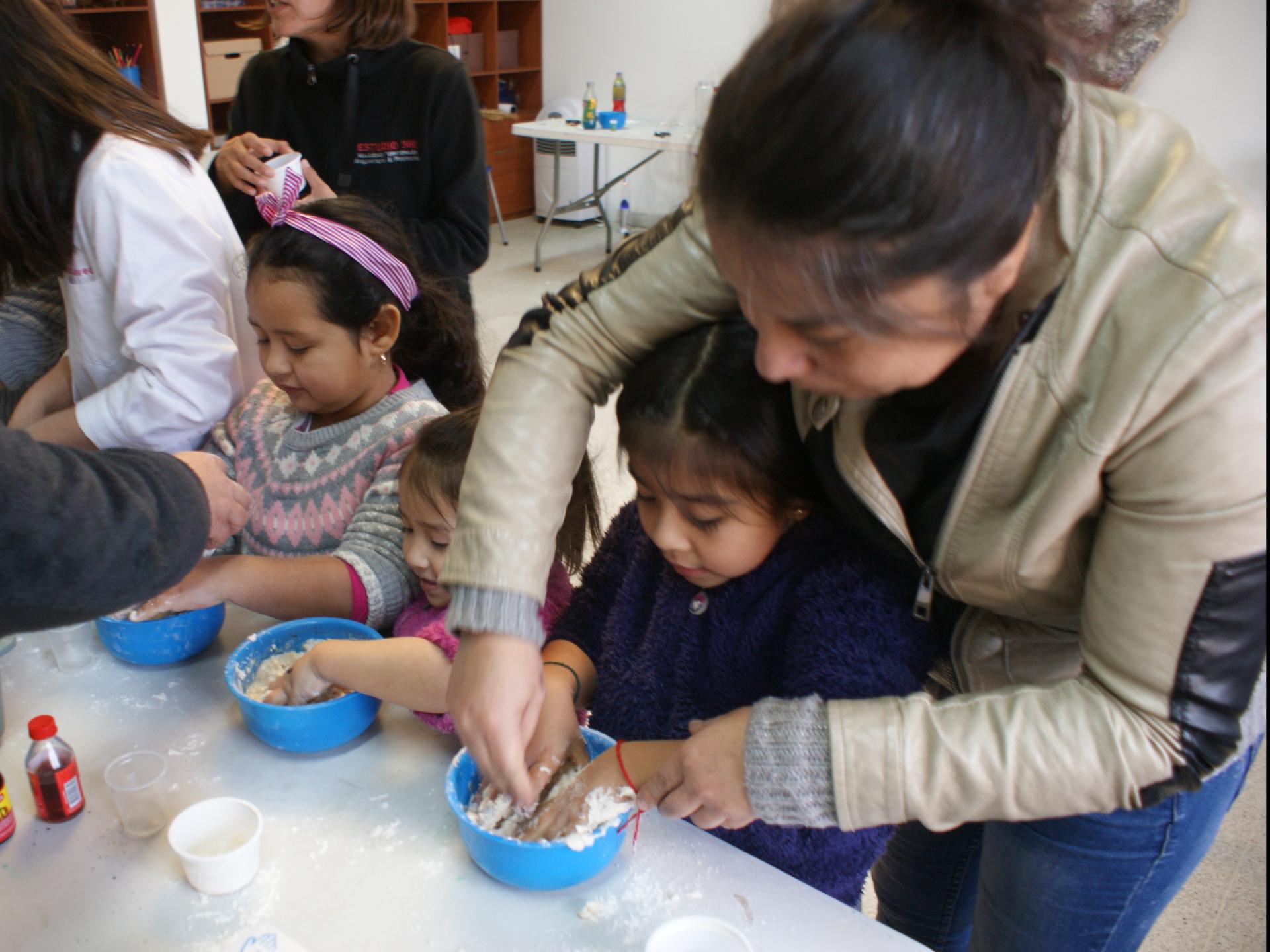 Registro fotográfico de un taller de invierno realizado el 2019. En la imagen se aprecia una niña pequeña junto a su madre amasando en un pequeño ball de plástico