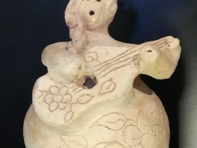 Artesanía en greda que representa una figura femenina tocando una guitarra