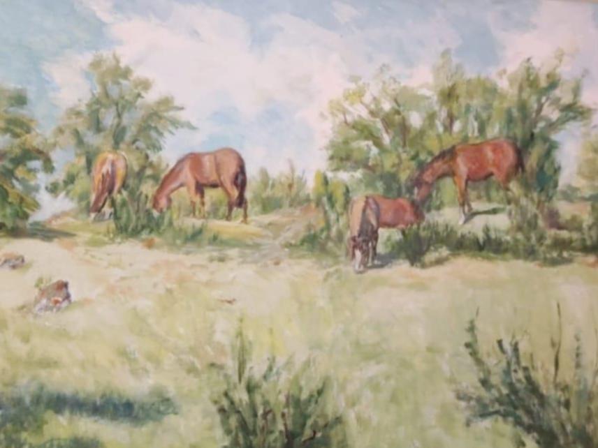 Paisaje de verdes praderas en que se aprecias un grupo de caballos pastando.