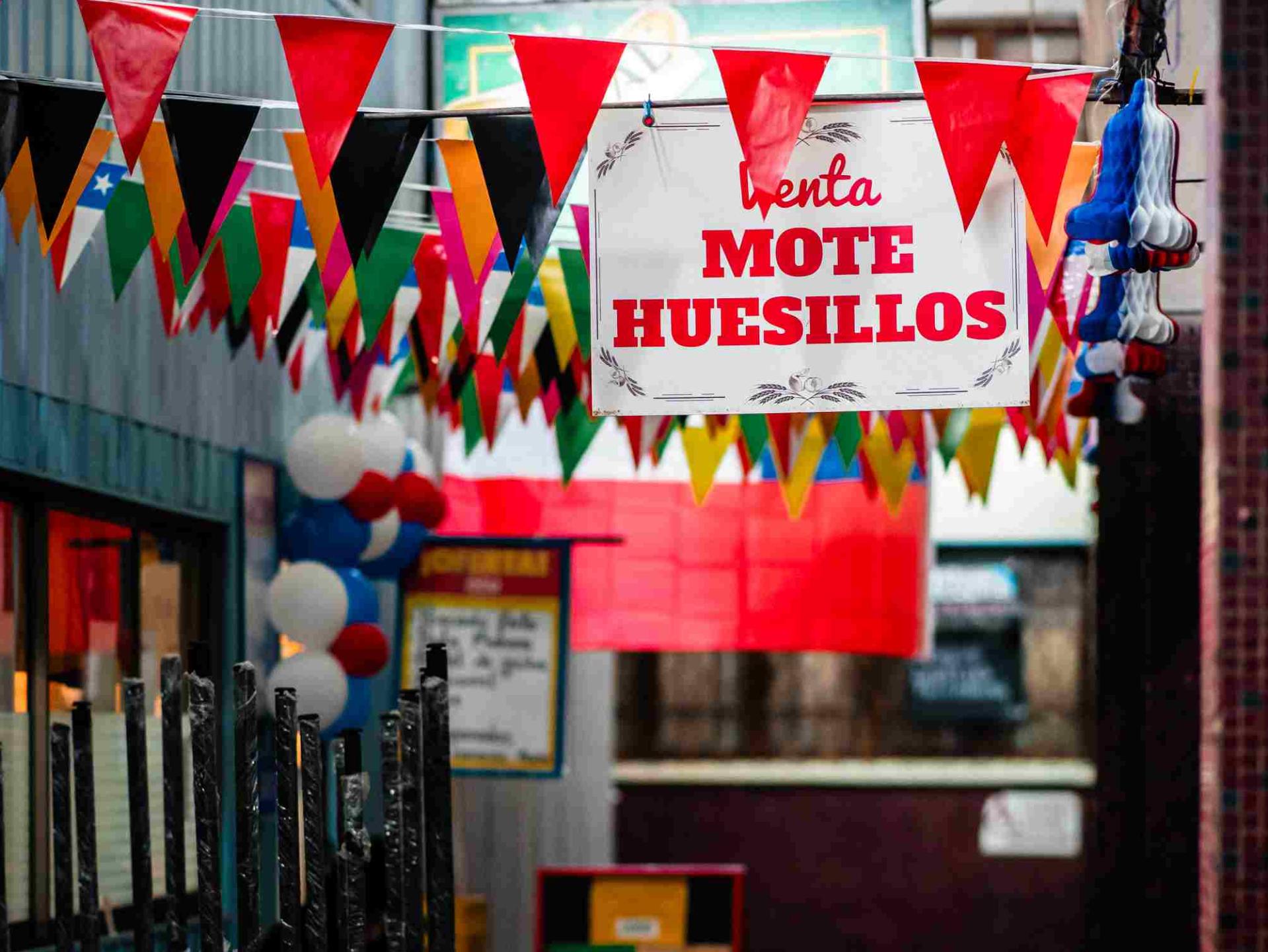 Muchos banderines de colores colgados y un letrero blanco con letras rojas que dice Mote con Huesillos
