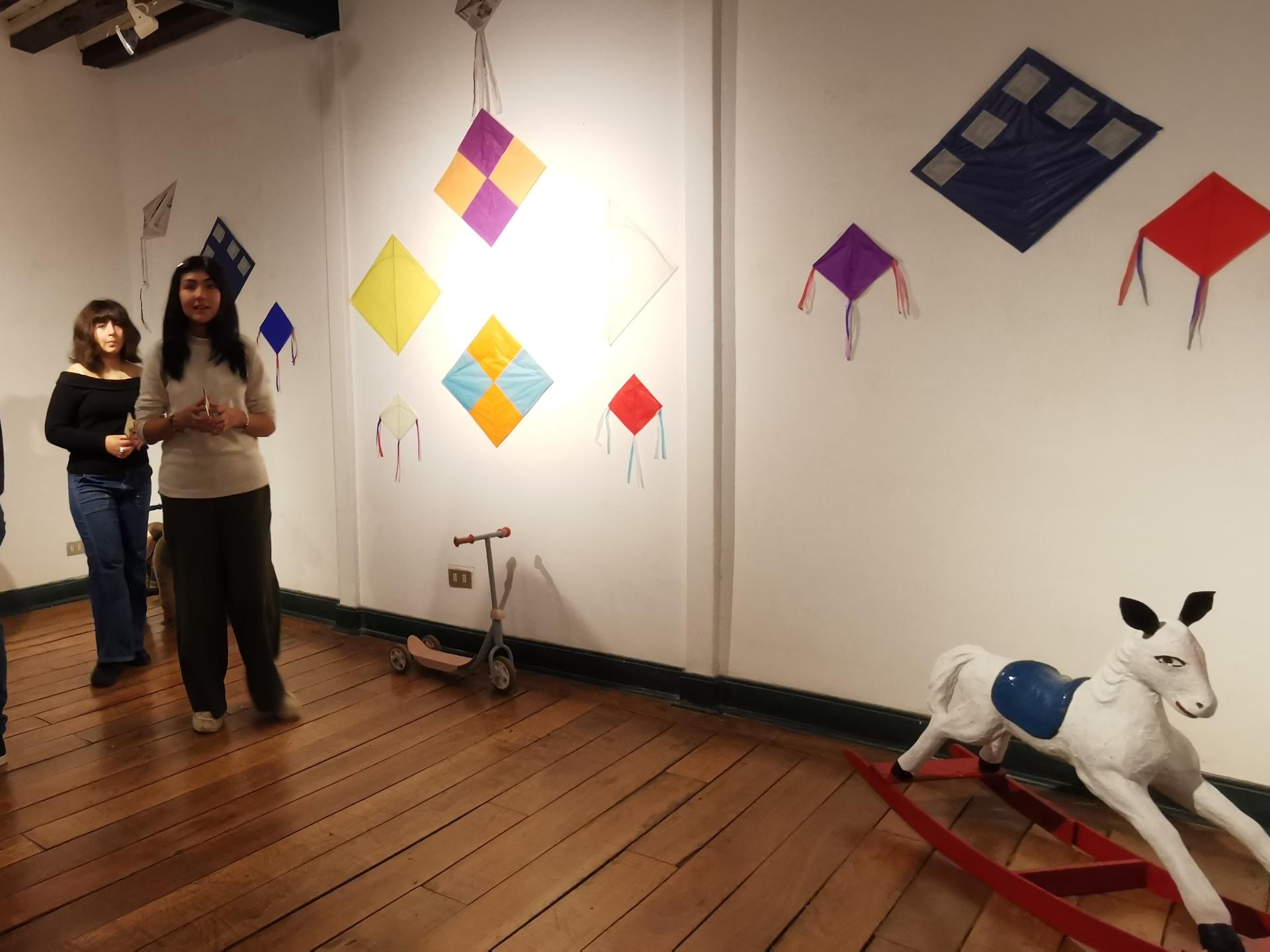 sala de exposición con personas, en la pared blanca se observan volantines de colores