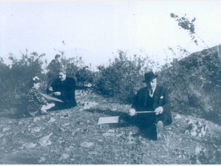 Fotografía monocromática que ilustra una escena en el cerro, compuesta por dos adultos y una niña sentados en el suelo preparando sus volantines.