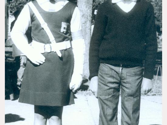Fotografía monocromatica compuesta por un niña y un niño vestidos de escolar, utilizando el uniforme de la bringada escolar (boina, guantes blancos y cinturon cruzado en su torzo).