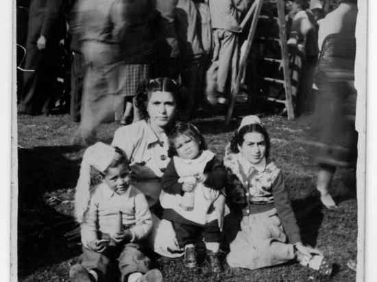 Fotografía monocromática, en el centro posa una mujer con un niño y dos niñas. De fondo se aprecia la multitud caminando en las ramadas de fiestas patrias.