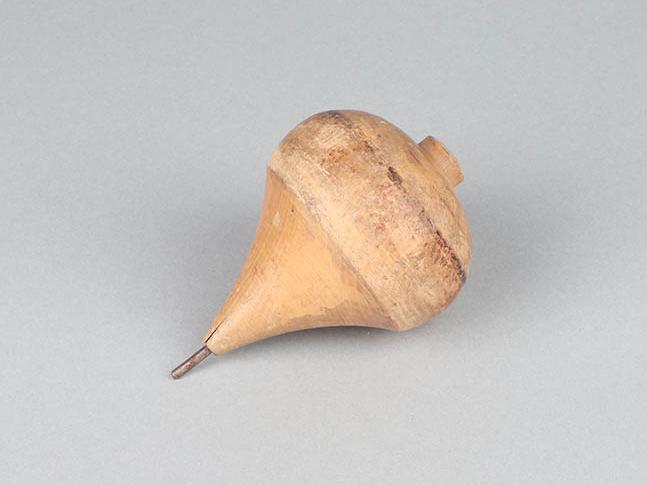 Imagen con fondo gris, en el centro una figura de madera que corresponde a un trompo.