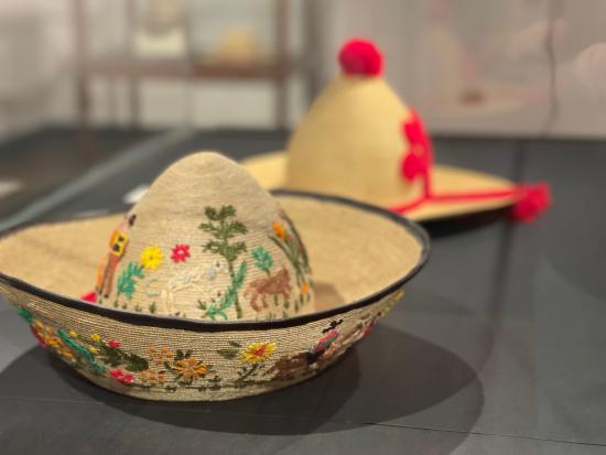 Fotografía que muestra un sombrero de paja de teatina tejida, su forma imita al bonete huicano, tanto en la parte externa del ala como en la copa posee coloridos bordados de lana con motivos costumbristas.