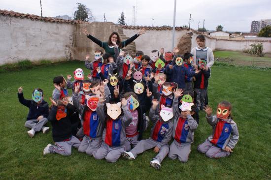 Grupos escolar de niñas y niños junto a educadoras de parvulo saludando a la cámara. Los niños y niñas llevan puesta máscaras de papel que representan fauna en riesgo presentes en la región tales como el loro tricahue, zorro cumpeo, ranita de darwin, entre otros.