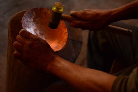 Fotografía que muestra una pieza de cobra en proceso de martillado, se aprecian unas manos golpeando la pieza con un martillo.