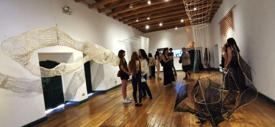 Sala de Exposición, con personas de pie conversando y las obras en exhibición