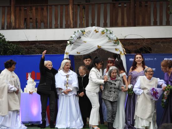 Mujeres ancianas y jóvenes vestidas de blanco con trajes de novia posan sobre un escenario