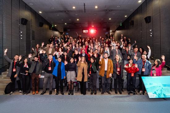 personas de pie en un teatro, saludan con la mano en alto