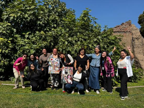 mujeres de pie frente a un arbol sonríen mientras posan para una foto y saludan a la camara