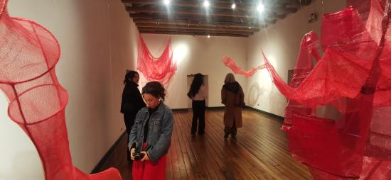 Sala de museo con esculturas aereas en color rojo y personas recorriendo la sala