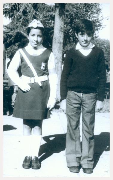 Fotografía monocromatica compuesta por un niña y un niño vestidos de escolar, utilizando el uniforme de la bringada escolar (boina, guantes blancos y cinturon cruzado en su torzo).
