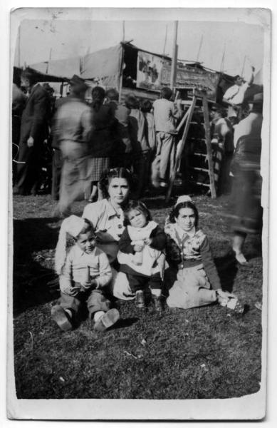 Fotografía monocromática, en el centro posa una mujer con un niño y dos niñas. De fondo se aprecia la multitud caminando en las ramadas de fiestas patrias.
