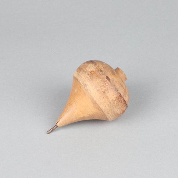 Imagen con fondo gris, en el centro una figura de madera que corresponde a un trompo.